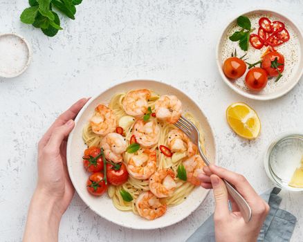 Pasta bavette with fried shrimps, bechamel sauce. Woman hands in frame, girl eats pasta, holds fork in hands, top view, italian cuisine.