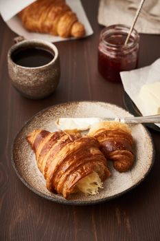Morning breakfast with croissant on plate, cup of coffee, jam and butter. Dark brown table , morning routine, slow life. Vertical, side view