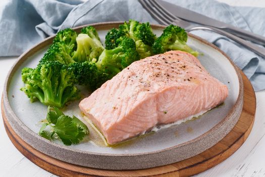 Steam salmon, broccoli, paleo, keto, lshf or dash diet. Mediterranean, Clean eating, balanced food. Gray ceramic plate on white table, side view