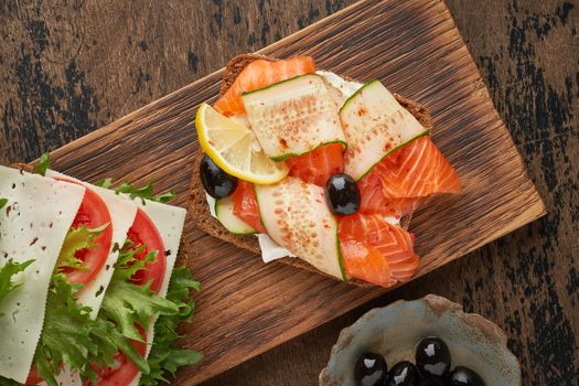Smorrebrod - traditional Danish sandwiches. Black rye bread with salmon, cream cheese, cucumber, tomatoes on dark brown wooden background, copy space