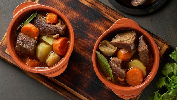 Goulash with large pieces of beef and vegetables. Burgundy meat. Slow stewing, cooking in pot or cast-iron pan. Dark backdrop