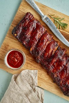 Barbecue pork ribs. Slow cooking recipe. Whole pickled roasted pork meat with red sauce on cutting board, vertical, top view. Turquoise background