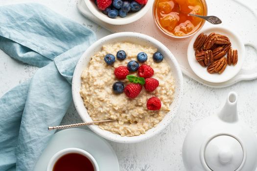 Oatmeal porridge with blueberry, raspberries, jam and nuts in white bowl, dash diet with berries, white background, top view. Healthy diet breakfast