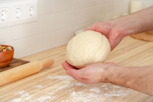 Faceless man kneading dough on kitchen table at home, apartment, flour, scales, bowls, digital tablet with recipes on table. Homemade food