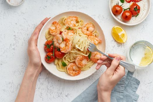 Pasta bavette with fried shrimps, bechamel sauce. Woman hands in frame, girl eats pasta, holds fork in hands, top view, italian cuisine.