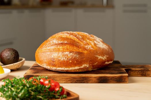 Whole loaf of freshly baked white wheat bread on wooden board on home kitchen table, copy space, side view