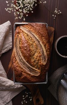 Banana bread. Cake with banana, traditional american cuisine. Whole loaf. Dark background, black table, shadows. Vertical, top view, close up.