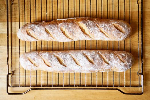 Fresh baked homemade crusty bread baguette. Two loaves cool on metal grate on wooden table. Delicious and healthy homemade loaf