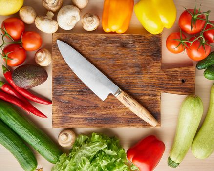 Vegetables around wooden cutting board with knife on kitchen table. Top view. Food ingredient background.