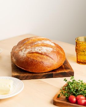 Whole loaf of freshly baked white wheat bread on wooden board on home kitchen table, vertical