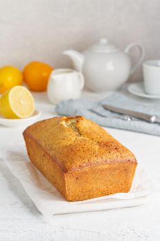Lemon bread. Cake with citrus and poppy on cutting board, traditional american cuisine. Whole loaf. White background, gray table. Vertical, side view, copy space