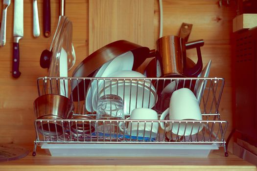 Clean washed dishes are laid out on dryer against background of a wooden wall of country house after breakfast