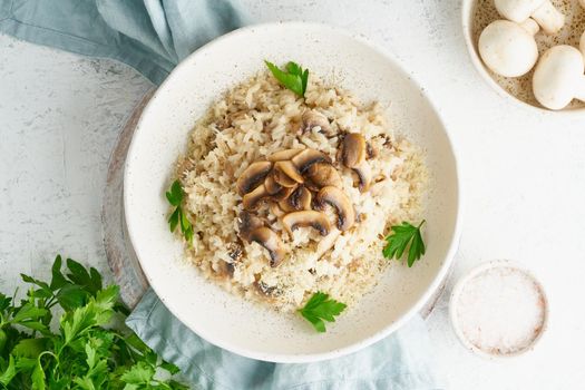 Risotto with mushrooms in plate. Rice porridge with mushrooms and parsley. White table, spoons, mushrooms. Hot dish, italian cuisine, top view