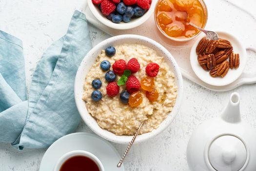 Oatmeal porridge with blueberry, raspberries, jam and nuts in white bowl, dash diet with berries, white background, top view. Healthy diet breakfast