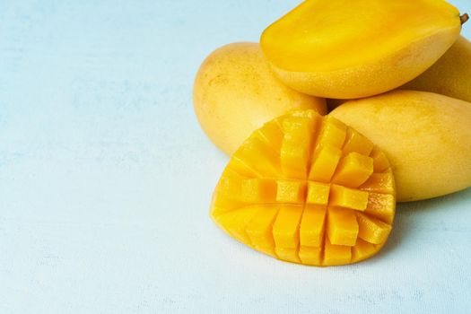 Four whole mango fruits on bright blue table and cut into slices. Large juicy bright ripe yellow fruits on color background, close up, copy space
