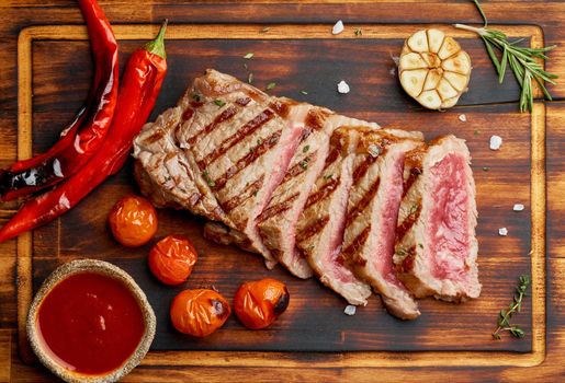 Keto ketogenic diet grilled fried beef steak, striploin on cutting board on dark brown table. Paleo food recipe with grilled fried chopped piece of meat, papper, top view, close up