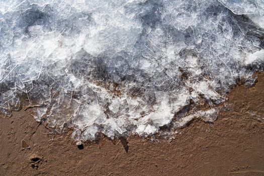 Ice on beach. Border of winter and summer. Ice and sand. Cold and warm. Contrast transition of seasons and weather, section