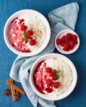 Rice pudding. French milk rice dessert with raspberries, blueberries, berries, jam. Healthy Vegan diet breakfast with coconut milk, cinnamon. Blue linen textile. Top view, vertical