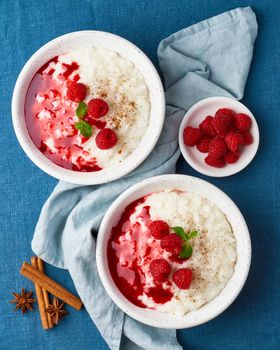 Rice pudding. French milk rice dessert with raspberries, blueberries, berries, jam. Healthy Vegan diet breakfast with coconut milk, cinnamon. Blue linen textile. Top view, vertical