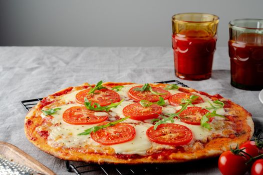 Rustic Italian homemade Pizza Dough margherita topped with pizza sauce from canned tomatoes, mozzarella cheese and arugula on dark linen textile tablecloth, side view