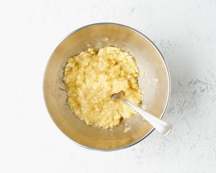 Homemade Banana bread. Dough for cake. Step by step recipe. Step 2. Mashed banana. Top view, white table.