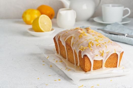 Lemon bread coated with sugar sweet icing and sprinkled with lemon peel. Cake with citrus, poppy, traditional american cuisine. Whole loaf. White background, side view, copy space