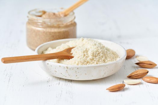Alternative almond flour. Grated crushed almonds, chopped in a blender, plate, spoon, nuts on the table. White background, side view, close up