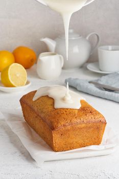 Lemon bread. Process of coating with sugar sweet glaze, stream of glaze flows. Cake with citrus, poppy, traditional american cuisine. Whole loaf. White background, side view, copy space