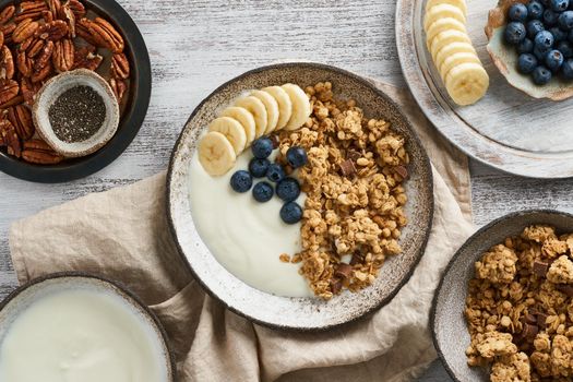 Yogurt with chocolate granola, bilberry. Breakfast, healthy diet food with oat flakes, nuts, banana, rustic wooden table, top view