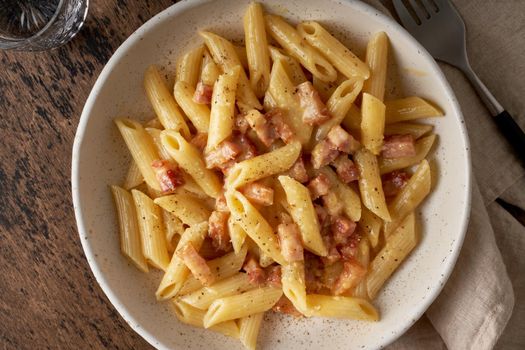 Carbonara pasta. Penne with pancetta, egg, parmesan cheese and cream sauce. Traditional italian cuisine. Top view, close up