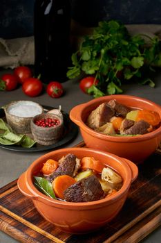 Goulash with large pieces of beef and vegetables. Burgundy meat. Slow stewing, cooking in two pot or cast-iron pan. Dark backdrop. Vertical