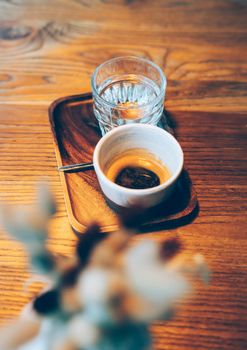Cup of espresso and glass of water on wooden table in cozy little cafe. High angle view, defocused, focus on background