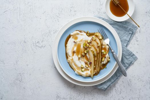 Ricotta with pears, pistachios and honey or maple syrup on blue plate on white table. Sweet and healthy dessert. Copy space