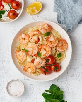 Pasta bavette with fried shrimps, bechamel sauce, mint leaf, garlic, tomatoes, chili on white plate, top view, italian cuisine. Vertical