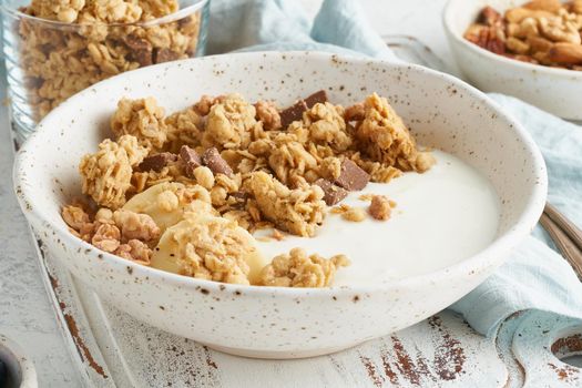 Yogurt with Granola. Breakfast, healthy diet food with oat flakes, nuts, banana, white table. Side view, close up
