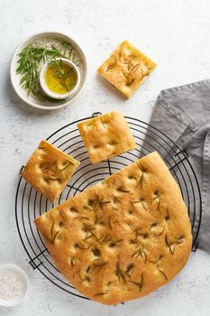 Focaccia, pizza, italian flat bread with rosemary and olive oil on grid on white rustic table, tradition italian cuisine, top view, vertical