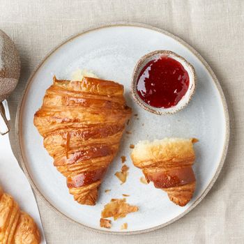 One delicious croissants on plate and hot drink in mug. Morning French breakfast with fresh pastries and jam. Light gray background, top view