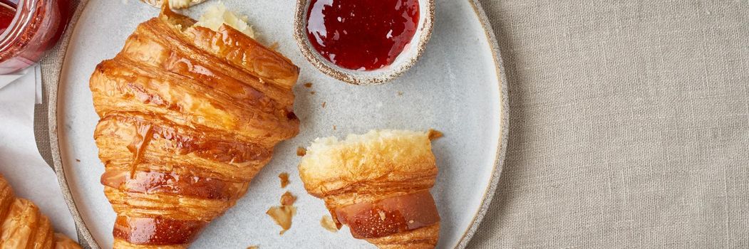 Long bannder with delicious croissants on plate and hot drink in mug. Morning French breakfast with fresh pastries and jam. Light gray background, top view