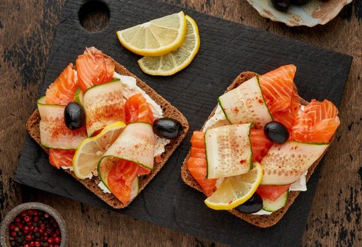 Smorrebrod - traditional Danish sandwiches. Black rye bread with salmon, cream cheese, cucumber and olives on dark brown wooden background