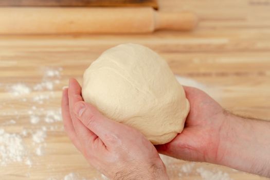 Faceless man kneading dough on kitchen table at home, apartment, flour, scales, bowls, digital tablet with recipes on table. Homemade food