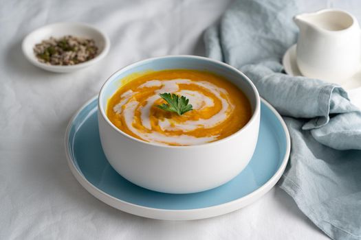 Pumpkin soup with coconut milk in blue bowl, vegetarian dish, healthy dieting food on white tablecloth, side view