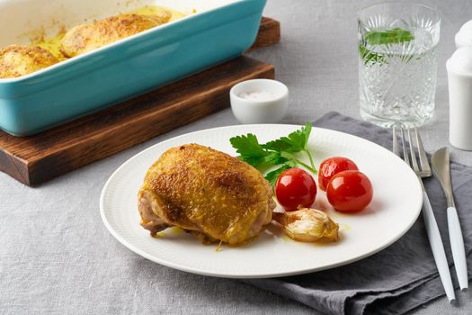 Chicken thighs baked with turmeric, tomatoes and garlic. Fried chicken is on plate, gray tablecloth, tray of meat. Healthy diet, clean eating, paleo, keto, ketogenic