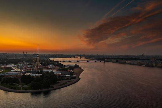 The Peter and Paul Fortress at sunrise, reflection of the orange and pink sky on the water, drawbridges Troitsky and Liteiny are separated. High quality photo