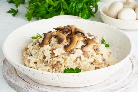 Risotto with mushrooms in plate. Rice porridge with mushrooms and parsley. White table, spoons, mushrooms. Hot dish, italian cuisine, side view