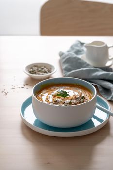 Pumpkin soup with coconut milk and seeds in blue bowl, vegetarian healthy dieting food on wooden background, vertical