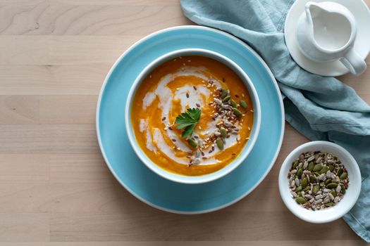 Pumpkin soup with coconut milk in blue bowl, vegetarian healthy dieting food on wooden background, top view, copy space