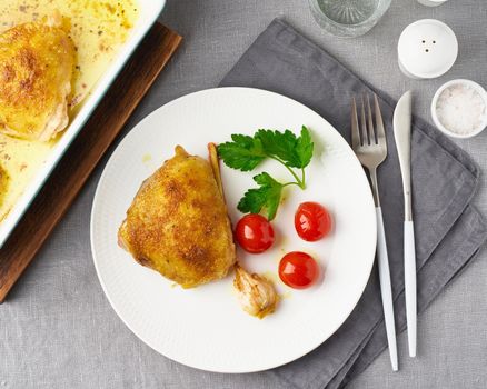 Chicken thighs baked with turmeric, tomatoes and garlic. Fried chicken is on plate, gray tablecloth, tray of meat. Healthy diet, clean eating, paleo, keto, ketogenic