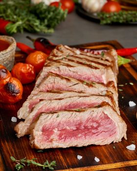 Keto ketogenic diet grilled fried beef steak, striploin on cutting board on dark brown table. Paleo food recipe with grilled fried chopped piece of meat, papper, side view, close up