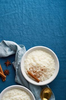 Rice pudding. French milk rice dessert. Healthy Vegan diet breakfast with coconut milk, cinnamon. Blue linen textile. Dark background. Top view, vertical, copy space