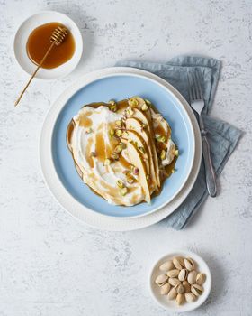 Ricotta with pears, pistachios and honey or maple syrup on blue plate on white table. Sweet and healthy dessert. Vertical